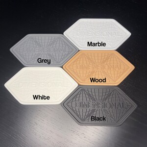 May include: A collection of five hexagonal coasters in various colors: grey, marble, wood, white, and black. Each coaster features a globe design with the word "DIMENSIONAL" and the color name printed on it.