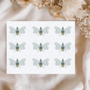 Puede incluir: Una tarjeta blanca con un patrón repetido de abejas estilizadas. Cada abeja tiene alas detalladas, un cuerpo azul-verdoso y un abdomen amarillo. El diseño es delicado e inspirado en la naturaleza.