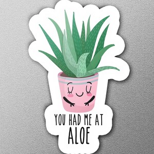 May include: A pink pot with a smiling face holds a green aloe plant. The text "You had me at aloe" is written below the pot.
