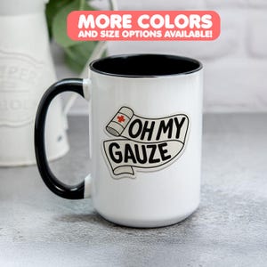 Könnte beinhalten: Weißer Keramikbecher mit schwarzem Henkel und Rand. Der Becher zeigt den Text "OH MY GAUZE" mit einer Bandagen-Grafik. Ein Banner oben lautet "MORE COLORS AND SIZE OPTIONS AVAILABLE!"