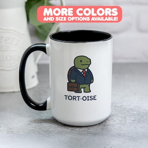 Pode incluir: Caneca de cerâmica branca com alça e interior pretos. A caneca apresenta uma tartaruga de desenho animado usando um terno e segurando uma pasta, com a palavra "TORT-OISE" abaixo. O texto na parte superior diz "MAIS CORES E OPÇÕES DE TAMANHO DISPONÍVEIS!"