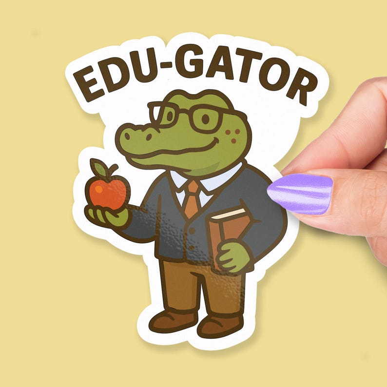 May include: A sticker featuring a cartoon alligator wearing glasses, a suit, and holding an apple and a book. The sticker has the text "EDU-GATOR" in brown letters. The alligator is green, and the apple is red.