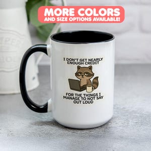 May include: White ceramic mug with a black handle and rim. The mug features a raccoon graphic with the text "I DON'T GET NEARLY ENOUGH CREDIT FOR THE THINGS I MANAGE TO NOT SAY OUT LOUD".