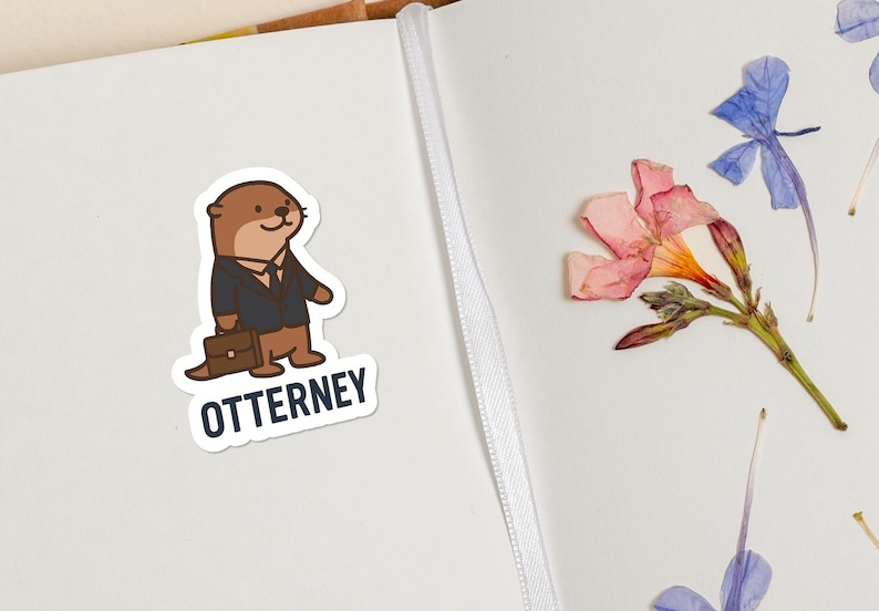 K&ouml;nnte beinhalten: Ein Aufkleber mit einem Cartoon-Otter im Anzug, der eine Aktentasche h&auml;lt, mit dem Wort "OTTERNEY" darunter. Der Aufkleber befindet sich auf einer wei&szlig;en Oberfl&auml;che neben getrockneten Blumen.