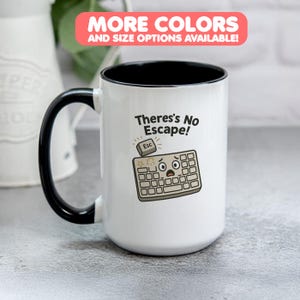 May include: White ceramic mug with a black handle and interior. The mug features the text "There's No Escape!" and a cartoon keyboard with an "Esc" key. The top of the mug has a red banner that says "MORE COLORS AND SIZE OPTIONS AVAILABLE!"