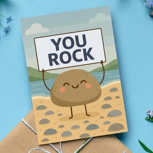 May include: A greeting card with a cartoon rock character holding a sign that reads "YOU ROCK." The rock has a smiling face and is standing on a beach scene with a blue sky and water.