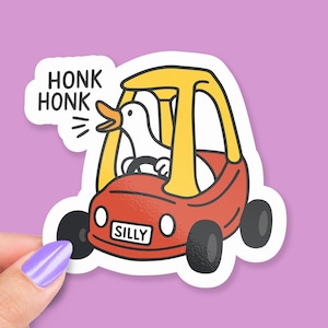Op de afbeelding: Een sticker met een witte eend die in een rode en gele speelgoedauto rijdt. Op de nummerplaat van de auto staat "SILLY". De sticker bevat ook de woorden "HONK HONK" in een tekstballon.