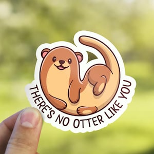 Peut inclure: Un autocollant blanc avec une loutre de dessin animé enroulée en cercle. La loutre est brune avec un ventre blanc et un visage mignon. Le texte "There's no otter like you" est écrit autour de la loutre dans un cercle blanc.