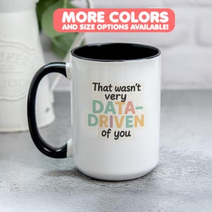 Peut inclure: Mug en céramique blanche avec une anse et un intérieur noirs. Le mug affiche le texte "That wasn't very DATA-DRIVEN of you" en plusieurs couleurs. Une bannière en haut indique "MORE COLORS AND SIZE OPTIONS AVAILABLE!"