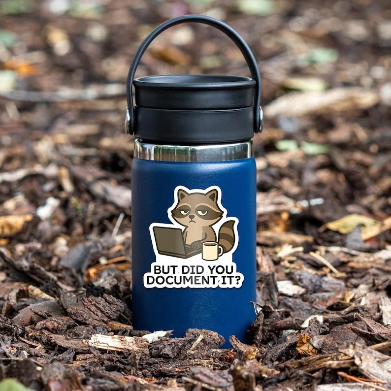 Puede incluir: Una botella de agua aislada azul oscuro con asa y tapa negras. Una pegatina en la botella presenta un mapache con un port&aacute;til y una taza de caf&eacute;, con el texto "BUT DID YOU DOCUMENT IT?"