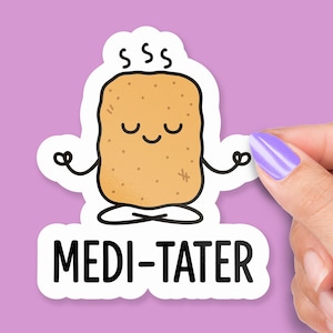 May include: A white sticker featuring a cartoon potato meditating. The potato is light brown with a smiling face and the text "MEDI-TATER" in black. The sticker is held by a hand with purple nail polish against a purple background.