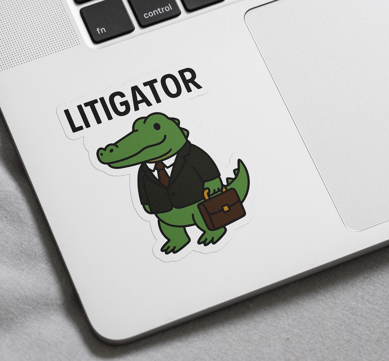 Pode incluir: Um autocolante com um jacar&eacute; de desenho animado de fato, segurando uma maleta. A palavra "LITIGATOR" est&aacute; impressa acima do jacar&eacute; em letras mai&uacute;sculas pretas. O jacar&eacute; &eacute; verde com um fato preto e uma maleta castanha.
