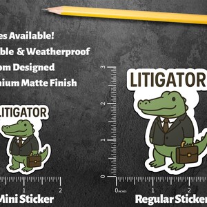 Pode incluir: S&atilde;o exibidos dois adesivos, um com a etiqueta "Mini Sticker" e o outro "Regular Sticker". Ambos apresentam um jacar&eacute; de desenho animado de terno segurando uma pasta, com a palavra "LITIGATOR" acima. Os adesivos est&atilde;o em um fundo escuro.