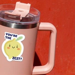 May include: A pink stainless steel travel mug with a lid and a lemon sticker that says "You're the Zest!"