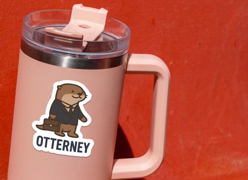 K&ouml;nnte beinhalten: Ein rosa isolierter Becher mit Griff und transparentem Deckel. Auf dem Becher befindet sich ein Aufkleber eines Cartoon-Otters im Anzug mit einer Aktentasche. Der Aufkleber tr&auml;gt das Wort "OTTERNEY" in wei&szlig;er Schrift.
