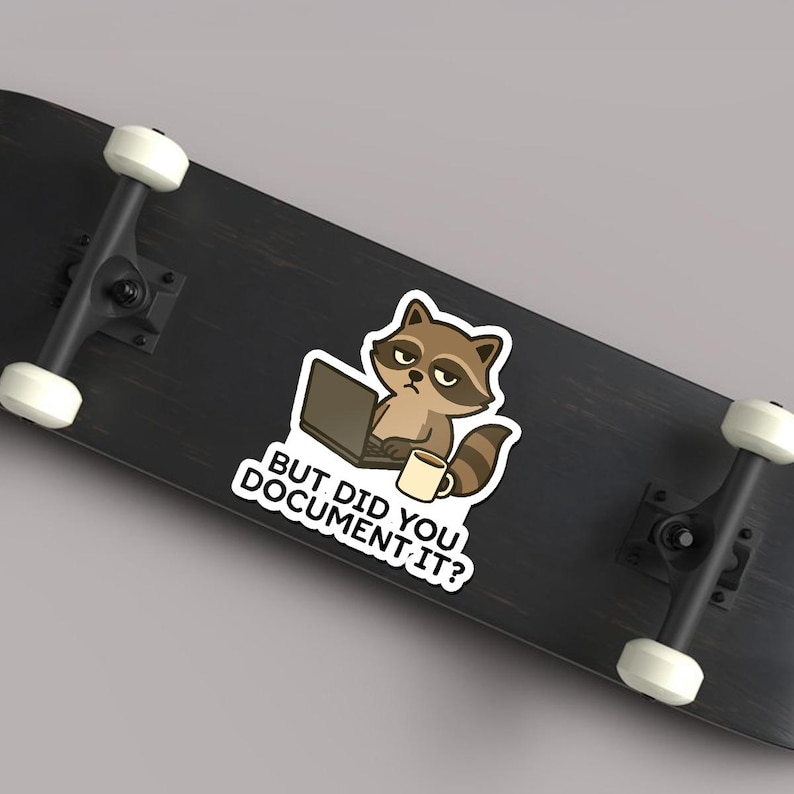 Puede incluir: Una pegatina con un mapache de dibujos animados con un port&aacute;til y una taza de caf&eacute;. El mapache tiene una expresi&oacute;n de mal humor y el texto "BUT DID YOU DOCUMENT IT?" est&aacute; debajo. La pegatina est&aacute; sobre una patineta negra.