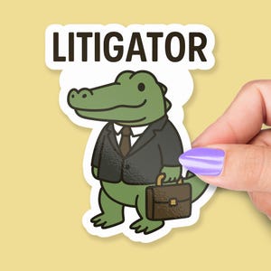 Pode incluir: Um adesivo com um jacar&eacute; de desenho animado em um terno preto, gravata e carregando uma pasta. A palavra "LITIGATOR" &eacute; impressa acima do jacar&eacute; em letras marrons escuras. O jacar&eacute; &eacute; verde com um fundo branco.