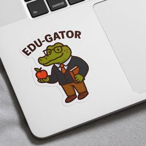 May include: A sticker featuring a cartoon alligator wearing glasses, a suit, and holding a book and a red apple. The sticker has the text "EDU-GATOR" in a speech bubble above the alligator.