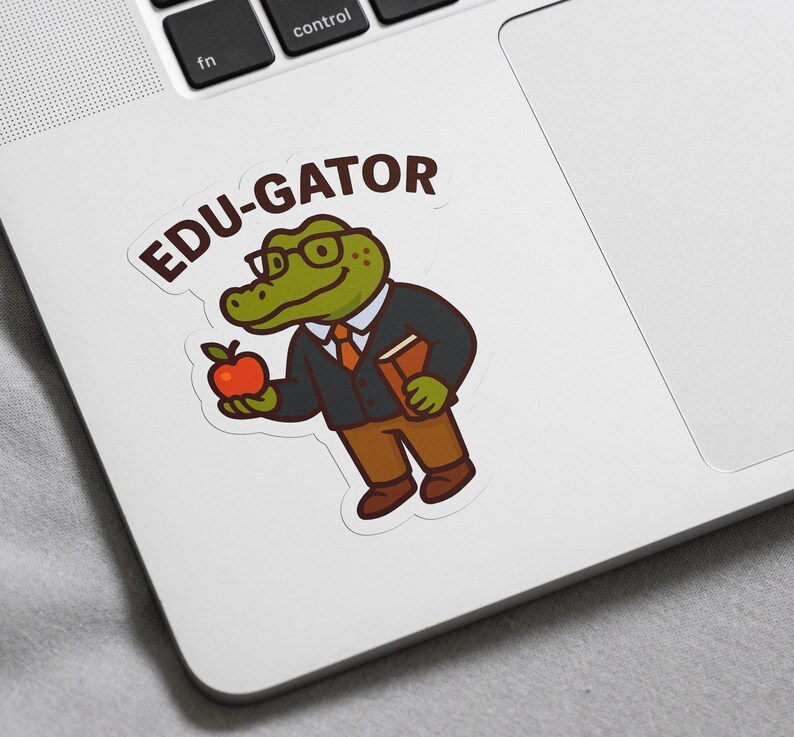 May include: A sticker featuring a cartoon alligator wearing glasses, a suit, and holding a book and a red apple. The sticker has the text "EDU-GATOR" in a speech bubble above the alligator.