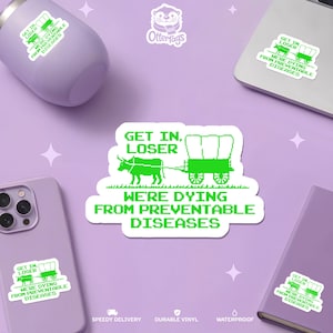 May include: A collection of green and white stickers with the text "GET IN, LOSER, WE'RE DYING FROM PREVENTABLE DISEASES." The stickers feature a pixelated image of a covered wagon pulled by a bull. Other items in the image include a purple tumbler, phone, laptop, and notebook.