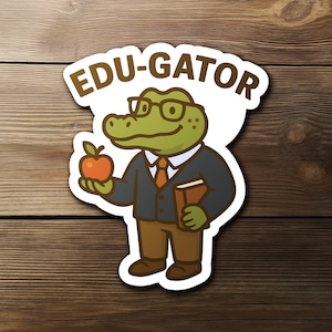 May include: A sticker featuring a cartoon alligator wearing glasses, a suit, and holding an apple and a book. The sticker has the text "EDU-GATOR" in brown letters on a white background.