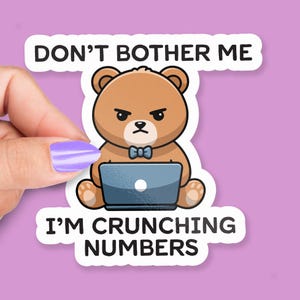 Könnte beinhalten: Ein Aufkleber mit einem braunen Bären, der einen Laptop benutzt und einen wütenden Gesichtsausdruck hat. Der Aufkleber trägt den Text "DON'T BOTHER ME" über dem Bären und "I'M CRUNCHING NUMBERS" darunter.