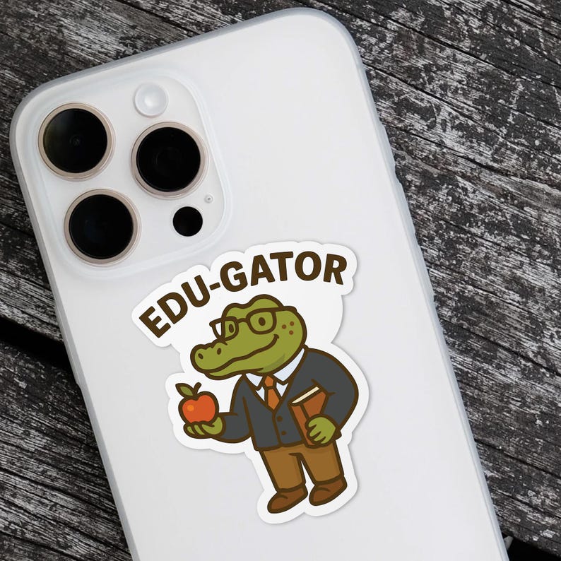 May include: A sticker featuring a cartoon alligator wearing glasses, a suit, and holding an apple and a book. The sticker has the text "EDU-GATOR" in a speech bubble. The sticker is on a white phone case.
