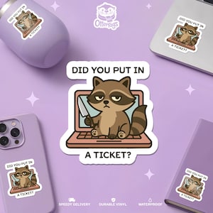 Könnte beinhalten: Ein Aufkleber mit einem Cartoon-Waschbären, der ein Messer hält und auf einem Laptop sitzt, mit dem Text "DID YOU PUT IN A TICKET?". Das Bild wiederholt sich auf einem Becher, Laptop, Telefon und Notizbuch.