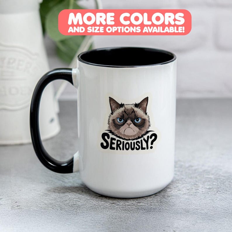 May include: A white ceramic mug with a black handle and rim. The mug features a graphic of a grumpy cat with the word "SERIOUSLY?" below. The text "MORE COLORS AND SIZE OPTIONS AVAILABLE!" is in a pink rectangle.