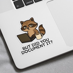 Puede incluir: Una pegatina con un mapache de dibujos animados con un port&aacute;til y una taza de caf&eacute;. El mapache tiene una expresi&oacute;n de mal humor. El texto de la pegatina dice: "BUT DID YOU DOCUMENT IT?" La pegatina est&aacute; en un port&aacute;til blanco.