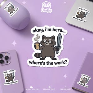 May include: A die-cut sticker featuring a cartoon raccoon holding a steaming cup of coffee in one hand and a grey sword in the other. The text above and below the raccoon reads, "okay, i'm here... where's the work?" in a bold, black sans-serif font.