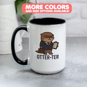 May include: White ceramic mug with a black interior and handle. The mug features a cartoon otter wearing glasses and a suit, holding a clipboard and briefcase. The text "OTTER-TER" is printed below the otter.