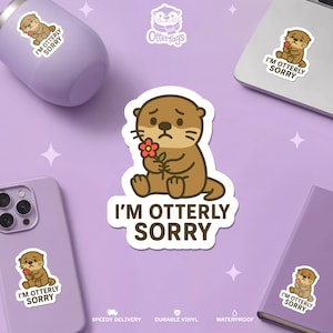 Könnte beinhalten: Eine Sammlung von Aufklebern und Accessoires mit einem Cartoon-Otter, der eine Blume hält, und dem Text "I'M OTTERLY SORRY". Die Artikel sind in Lila und Weiß gehalten, mit dem Ottertags-Logo.