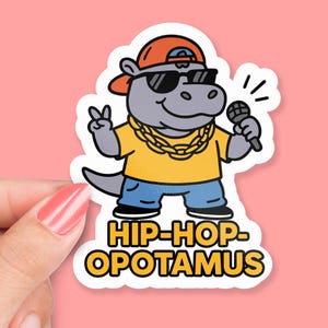 以下が含まれることがあります： サングラス、金のチェーン、野球帽を身に着けた漫画のヒポポタマスが描かれたステッカー。ヒポポタマスはマイクを持ち、ピースサインをしています。ステッカーには太字で「HIP-HOP-OPOTAMUS」と書かれています。