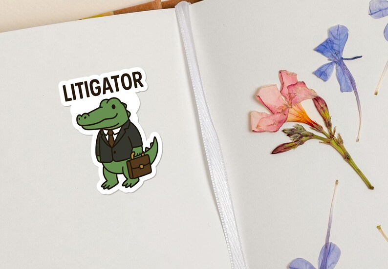 Pode incluir: Um autocolante com um jacar&eacute; de desenho animado vestido com fato e gravata, segurando uma pasta, com a palavra "LITIGATOR" por cima. A imagem tamb&eacute;m inclui flores secas. O autocolante est&aacute; numa superf&iacute;cie branca.
