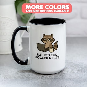 May include: White ceramic mug with a black handle and rim. The mug features a raccoon graphic with a laptop and coffee cup, and the text "BUT DID YOU DOCUMENT IT?" A banner at the top reads "MORE COLORS AND SIZE OPTIONS AVAILABLE!"