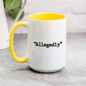 May include: White ceramic mug with a yellow interior and handle. The mug features the word "Allegedly" in black, centered on the front. The mug is on a light gray surface.