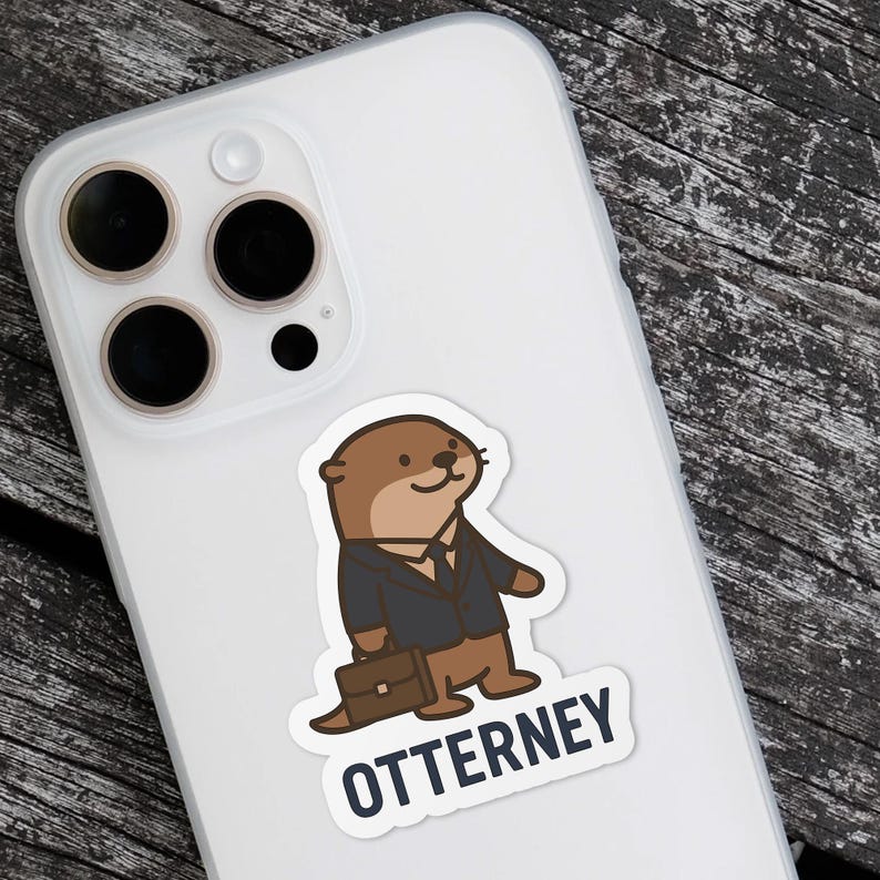 K&ouml;nnte beinhalten: Ein Aufkleber mit einem Cartoon-Otter in einem Anzug, der eine Aktentasche h&auml;lt. Der Otter ist braun und tr&auml;gt einen schwarzen Anzug. Der Text "OTTERNEY" steht darunter in Wei&szlig; mit blauem Rand. Der Aufkleber befindet sich auf einer wei&szlig;en Handyh&uuml;lle.