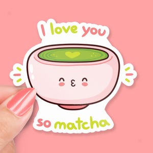 May include: A pink and green sticker with a cartoon illustration of a bowl of matcha tea. The bowl has a cute face and a heart in the tea. The text "I love you so matcha" is written below the bowl.
