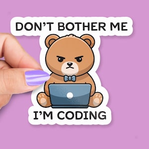 May include: A sticker featuring a brown cartoon bear with an angry expression, wearing a blue bow tie, and working on a blue laptop. The text "DON'T BOTHER ME" and "I'M CODING" are printed in black.