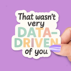 Pode incluir: Um autocolante com o texto "That wasn't very DATA-DRIVEN of you" numa fonte divertida. O autocolante tem uma borda branca e é segurado contra um fundo roxo. O texto é em várias cores pastel.