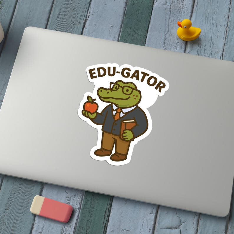 May include: A sticker featuring an alligator wearing glasses, a blazer, and a tie, holding an apple and a book. The sticker has the text "EDU-GATOR" in a bubble above the alligator's head. A yellow rubber duck is in the background.