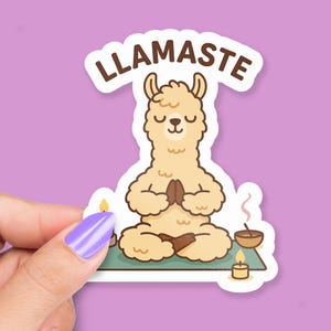 Op de afbeelding: Een sticker met een cartoon lama in een yogahouding, met het woord "LLAMASTE" erboven. De lama is lichtbruin, zittend op een groene mat, met kaarsen en een kom in de buurt. De achtergrond is effen paars.