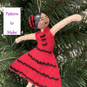 May include: A felt Christmas ornament of a dancer wearing a red dress with black trim. The ornament has a painted face and black hair with a red flower.