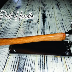 May include: A silver hammer with a wooden handle mounted on a black metal plate. The hammer has a textured head and the plate has two screws. The text "Pull Handle" is written in black on a white background.