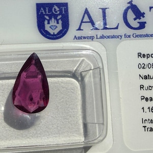 Könnte beinhalten: Ein birnenförmiger, facettierter Rubin in intensiver purpurroter Farbe, präsentiert in einem durchsichtigen Kunststoffgehäuse neben einer ALGT Antwerp Laboratory for Gemstone Testing Berichtskarte mit 1,16 Karat und natürlichem Korund.