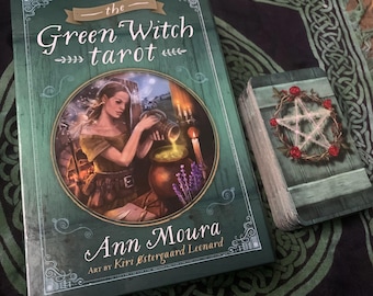 Może przedstawiać: Pudełko talii kart tarota Green Witch ma zielone tło z czarownicą mieszającą kocioł. Pudełko ma tytuł "The Green Witch Tarot" i nazwisko autorki "Ann Moura" wraz z nazwiskiem artystki "Kiri  Østergaard Leonard".