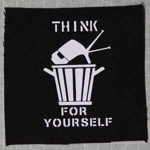 May include: Black fabric patch with white text and a graphic of a television in a trash can. The text reads "Think for yourself."
