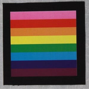 May include: A square patch with a rainbow design, featuring horizontal stripes in various colors: pink, red, orange, yellow, green, blue, indigo, and maroon. The rainbow design is framed by a black border.