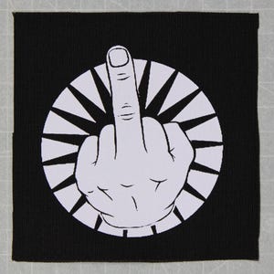 May include: Black and white iron-on patch with a white middle finger in a circle with a sunburst design.